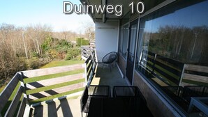 A balcony with a view of a grassy area and trees, a chair, and a table.