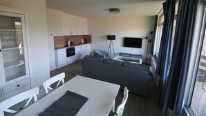 A modern kitchen with white cabinets, a built-in oven, and a dining area with a white table and chairs.