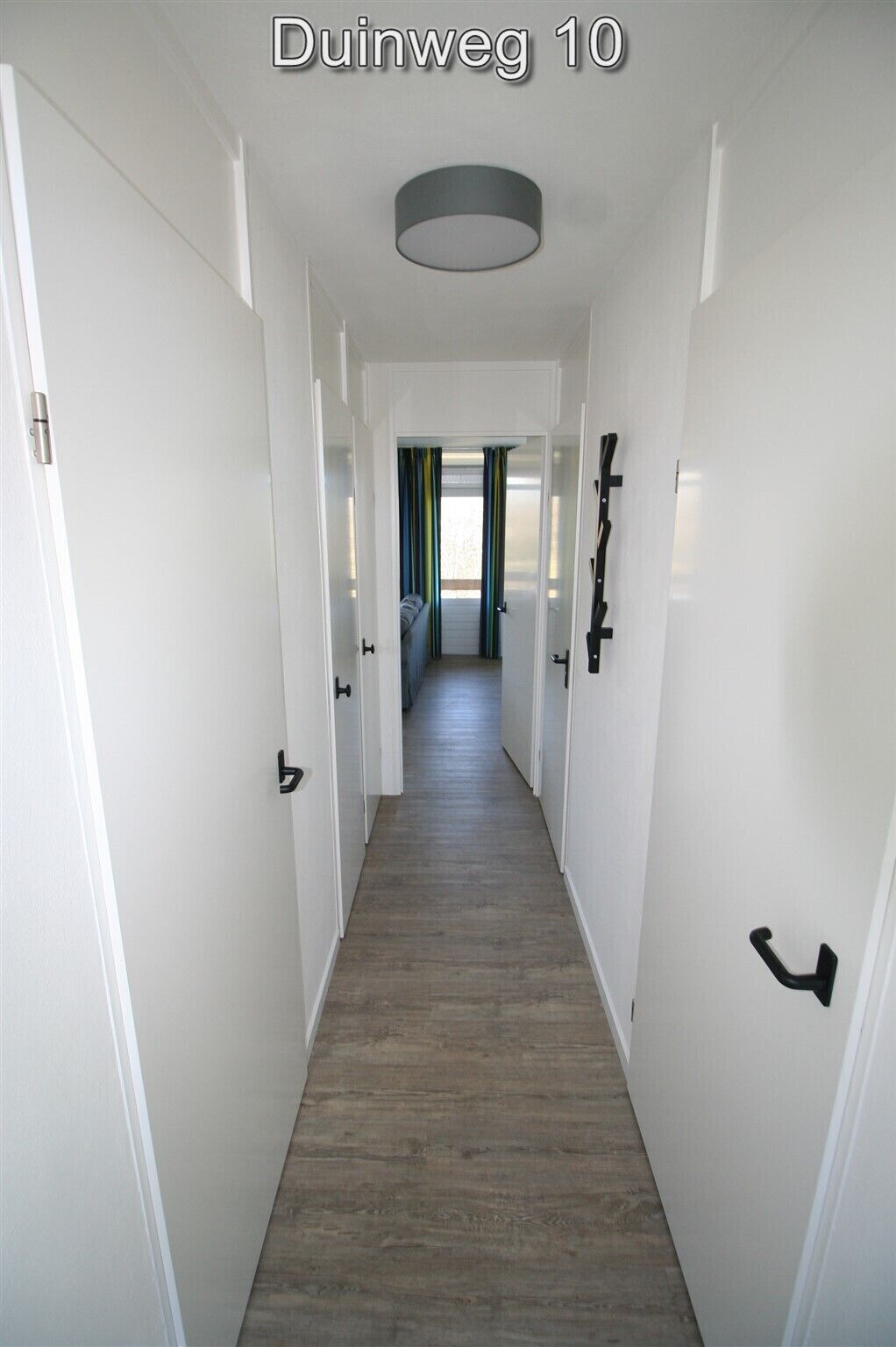 A hallway with white walls, wooden flooring, and black door handles.