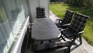 A patio with a table and four chairs, a window, and a grassy yard.