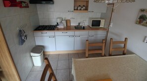 Une cuisine compacte équipée d’une cuisinière à gaz, d’un four à micro-ondes et d’un petit évier. On aperçoit une chaise et une table au premier plan.