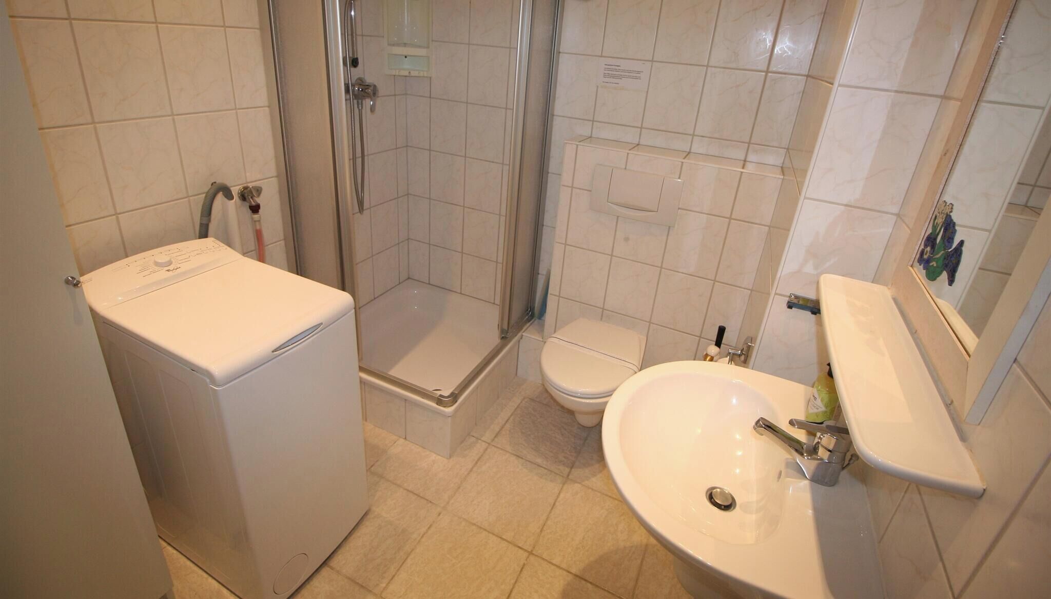 A bathroom with a shower, toilet, sink, and a washing machine.