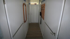 Un pasillo estrecho con suelo de madera, paredes blancas y puertas con tiradores de madera.