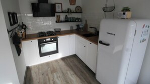 A compact kitchen with white cabinets, a black oven, a white refrigerator, and a wooden countertop. - 2 bedroom accommodation in Westkapelle (Westkapelle)