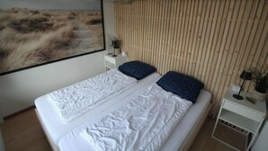 A bedroom with a bed, a nightstand, a lamp, and a wall-mounted painting. - 2 bedroom accommodation in Westkapelle (Westkapelle)