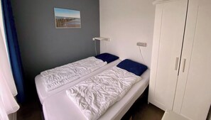 Ein Zimmer mit zwei Betten, einem Schrank, einer Wandleuchte und einem Bild.