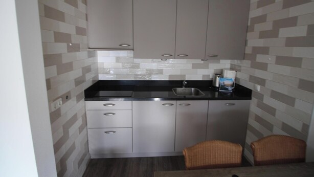 A compact kitchen with a black countertop, stainless steel cabinets, a sink, and a small wicker chair. - 3 bedroom accommodation in Westkapelle (Westkapelle)