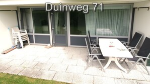 An outdoor patio with a table and chairs, a sliding glass door, and a stack of plastic chairs. - 3 bedroom accommodation in Westkapelle (Westkapelle)