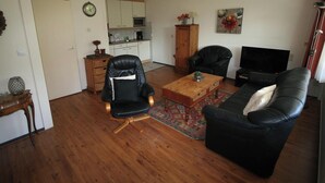 A living room with a black leather sofa, a wooden coffee table, a black leather armchair, and a television. - 2 bedroom accommodation in Westkapelle (Westkapelle)