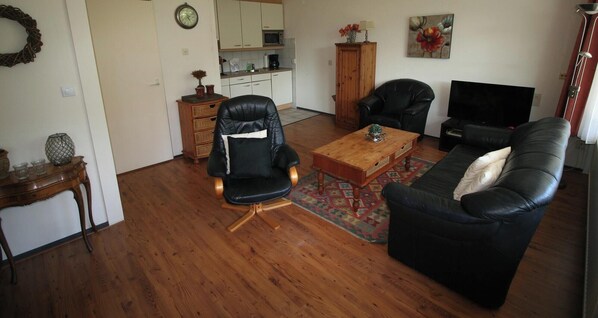 A living room with a black leather sofa, a wooden coffee table, a black leather armchair, and a television. - 2 bedroom accommodation in Westkapelle (Westkapelle)