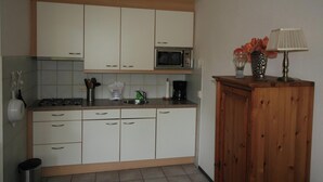 A kitchen with white cabinets, a microwave, a gas stove, a sink, and a wooden cabinet with a lamp. - 2 bedroom accommodation in Westkapelle (Westkapelle)