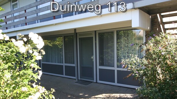 A modern building with large glass windows and a door, labeled 'Duinweg 113'. - 2 bedroom accommodation in Westkapelle (Westkapelle)
