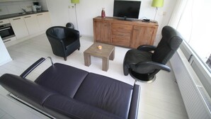 Ein Wohnzimmer mit einer Couch, einem Sessel, einem kleinen Tisch und einem Schrank mit einem Fernseher.