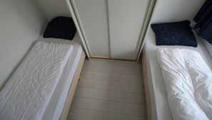 A small room with two single beds, a wooden floor, and a door leading to another room.