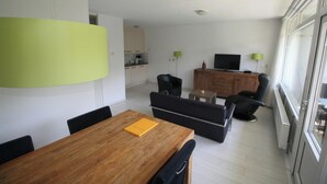 Ein modernes Wohnzimmer mit einem Holzespeisetisch, schwarzen Sofas und einem Fernseher auf einer Holzkommode.