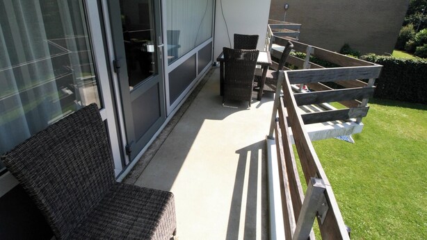 Ein Balkon mit Korbmöbeln, einer Holzbank und einer Rasenfläche.