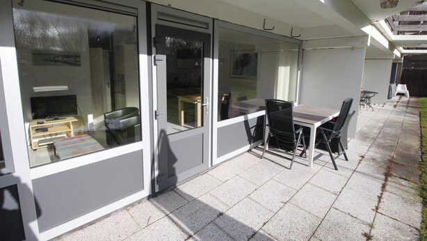 Eine Terrasse mit Tisch und Stühlen, einem Fernseher und einer Schiebetür.