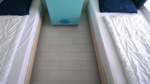 Ein Zimmer mit zwei Betten, einer kleinen blauen Kommode und einem hellen Holzboden.