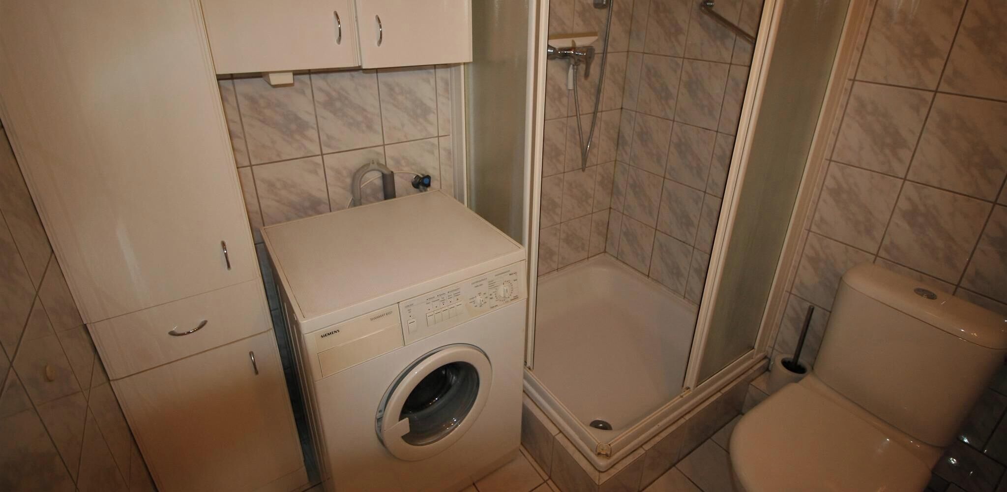 A compact bathroom with a washing machine, a shower enclosure, and a toilet.