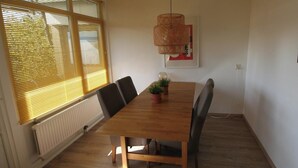 Ein Essbereich mit einem Holztisch, Stühlen, Topfpflanzen, einer Pendelleuchte und einem gerahmten Bild an der Wand.