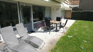 A patio area with a table and chairs, a grill, and a sliding glass door leading to a deck.