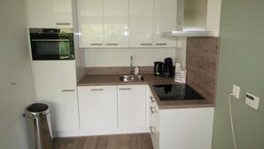 A compact kitchen with white cabinets, a stainless steel sink, a coffee maker, and a trash can.