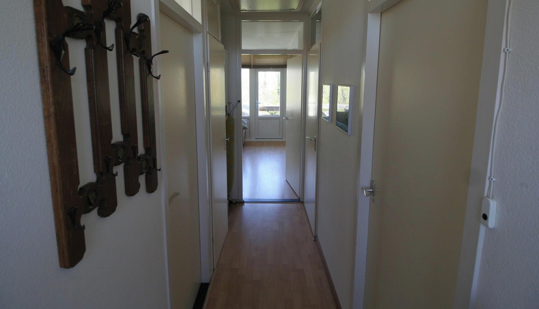 Un couloir étroit, avec des portes en bois et un porte-manteau sur le côté gauche.