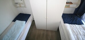 A small room with two single beds, a wardrobe, and a shelf with books.