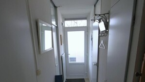 Ein schmaler Korridor mit weißen Wänden, einer Tür am Ende und einem Fenster mit Blick.