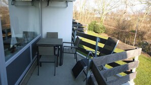 Ein Balkon mit Tisch, Stühlen, einer Glastür und Blick auf eine Rasenfläche mit Holzzaun.