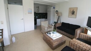 Ein Wohnzimmer mit einer schwarzen Couch, einem gestreiften Sessel, einem Korbsessel und einem kleinen Tisch mit Tablett.