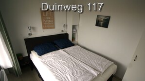 Ein Schlafzimmer mit Bett, Nachttisch, Wandregal, einem Poster und einem Bild an der Wand.
