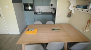 A compact kitchen with a built-in oven, a sink, and a small countertop. There is a wooden dining table with two chairs and a yellow folder on it.