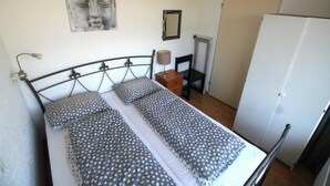 En säng med en metallram, två kuddar, ett sängbord, en lampa, en stol, en garderob och en vägg med en inramad tavla.
