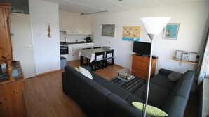 Ett kompakt bostadsutrymme med ett litet kök, en matplats, en soffa och en tv.