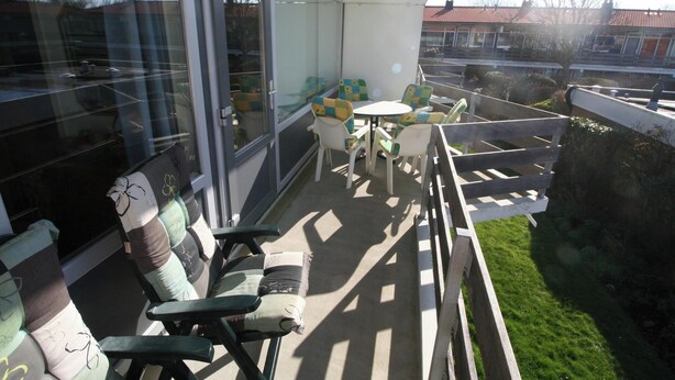 En balkong med utemöbler, en glasdörr och utsikt över ett bostadsområde.