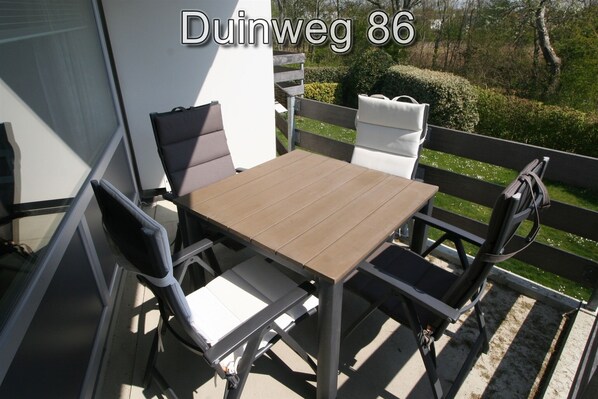 Une terrasse extérieure avec une table et des chaises, une clôture en bois et une vue sur un jardin.