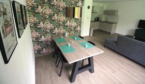 Un coin repas avec une table et des chaises en bois, une cuisine en arrière-plan et un canapé gris.
