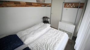 A bedroom with a bed, a chair, a dresser, and a mirror.