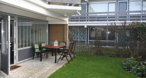 Une maison moderne dotée d’un patio, d’une table à manger avec des chaises et d’un petit jardin.