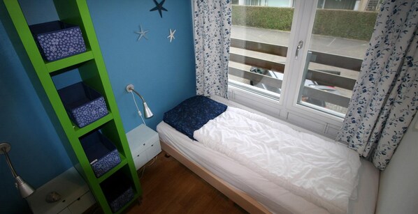 Une petite pièce avec un lit simple, un meuble de rangement vert, une fenêtre avec des rideaux et une décoration en forme d’étoile sur le mur.