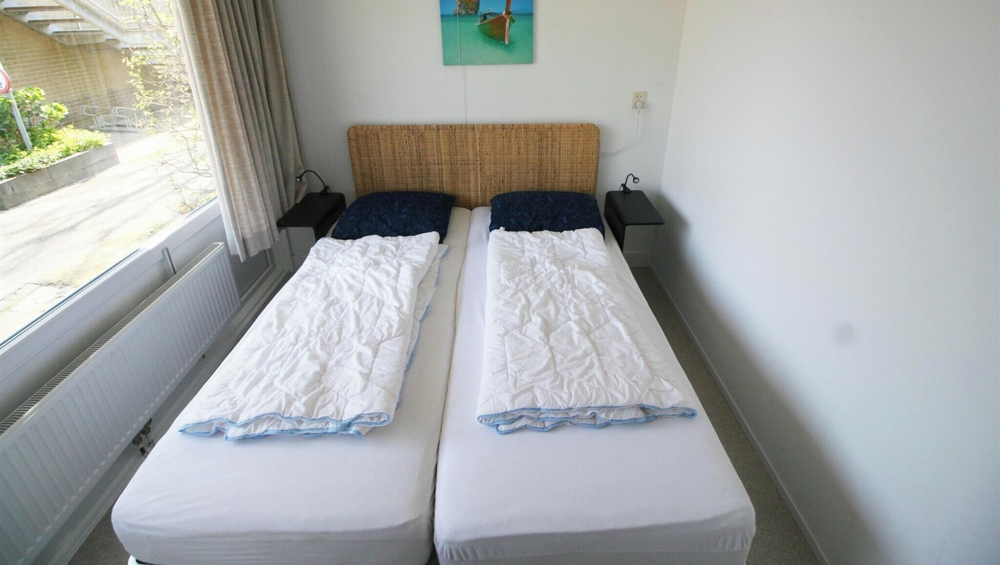 Una cama doble con cabecera de madera, dos mesitas de noche y una ventana con cortinas.