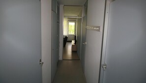 Ein schmaler Korridor mit geschlossenen Türen, einem Fenster am Ende und einer Tür mit Lichtschalter.