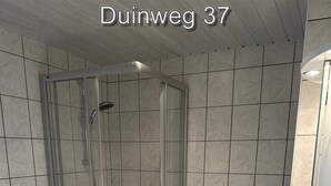 A bathroom with a glass-enclosed shower, a washing machine, and a sink.
