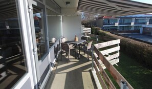 A balcony with a table and chairs, a wooden fence, and a view of a building in the background.