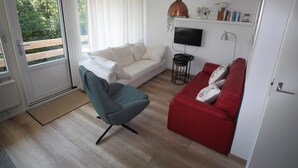 Un salon avec un canapé blanc, un canapé rouge, un fauteuil gris, un téléviseur et une petite table avec une lampe.