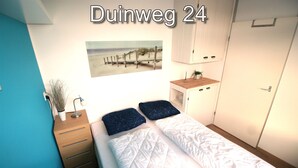 Une chambre à coucher avec un lit, une table de chevet, une petite table avec une plante, une armoire et un tableau sur le thème de la plage accroché au mur.