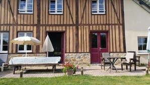 A traditional half-timbered building with a red door, a table with an umbrella, and outdoor seating. - Charming authentic Norman house with fireplace and pets allowed (Barenton)
