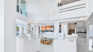 A spacious, modern living area with white furniture, a glass coffee table, and a view of the kitchen and pool. -  Villa NOVA (North Bay Village)
