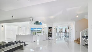 A spacious, modern living area with a large sofa, a dining table, and a kitchen visible through an open door. -  Villa NOVA (North Bay Village)